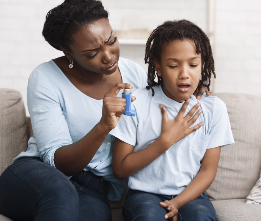 an individual and a young child sitting on a couch with an asthma inhaler